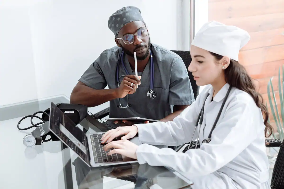 Doi medici discută un diagnostic la un laptop, într-un birou de spital