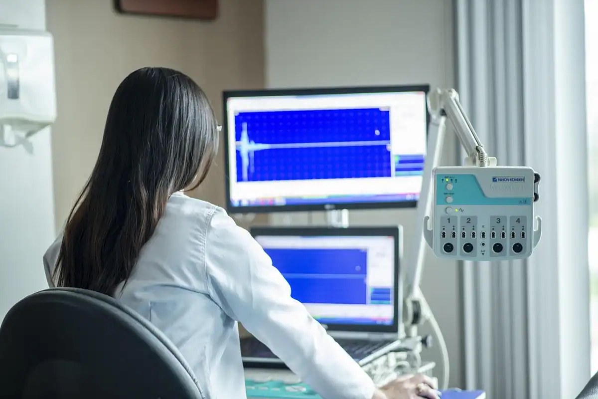 Specialistă în halat alb urmărește monitoare cu trasee medicale, lângă aparatura clinicii