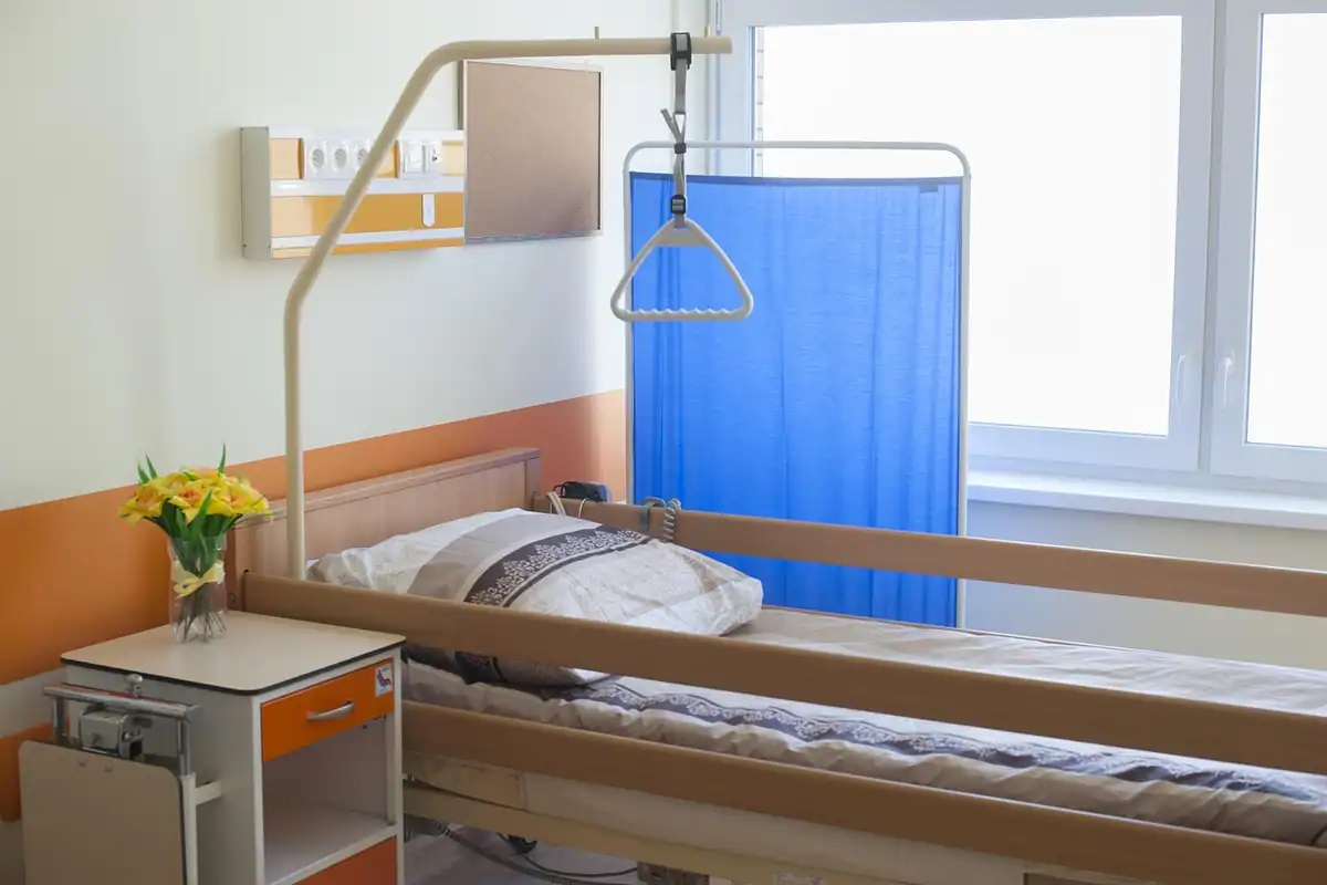 Salon de spital luminos cu pat reglabil, noptieră și paravan albastru pentru recuperare