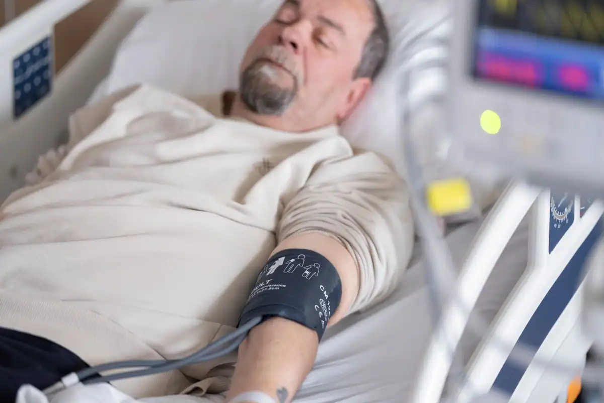 Bărbat în vârstă întins în patul de spital, cu tensiometru prins pe braț