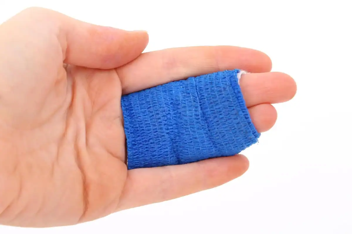 Mână care ține un bandaj elastic albastru înfășurat în jurul unui deget