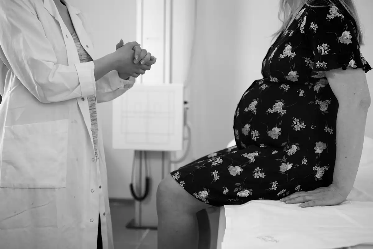 Medic în halat alb discută cu o femeie însărcinată, așezată pe patul de consultații