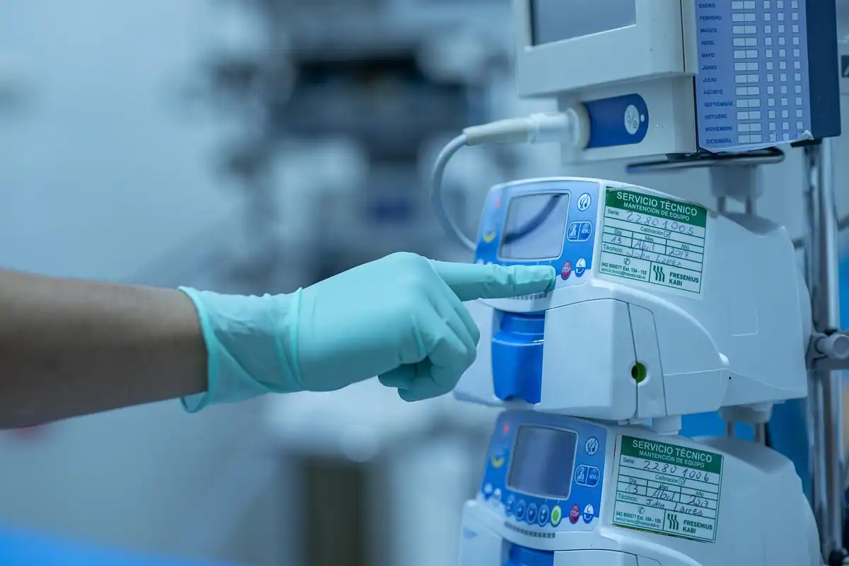 Mână cu mănușă albastră reglând o pompă de perfuzie într-un spital