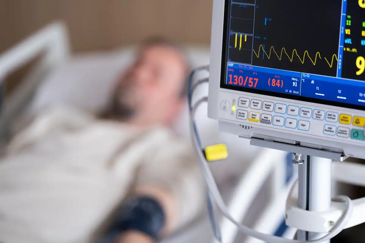 Monitor medical cu valorile tensiunii și pulsului, lângă un pacient culcat în pat