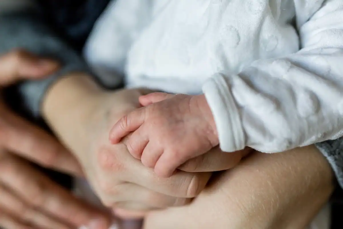 Mâna unui bebeluș strânsă în mâinile părinților, într-un gest de liniștire