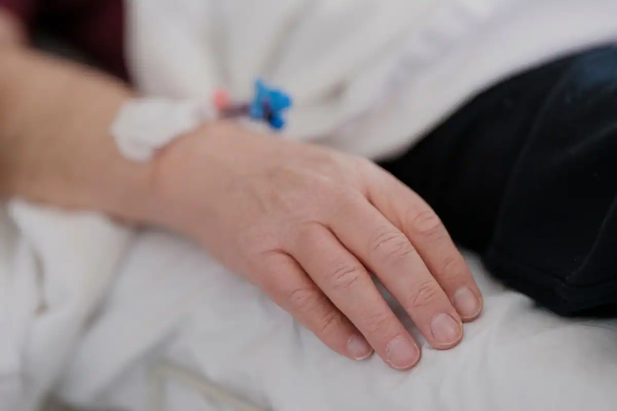 Mână de pacient pe pat, cu o branulă prinsă pentru administrarea sedării